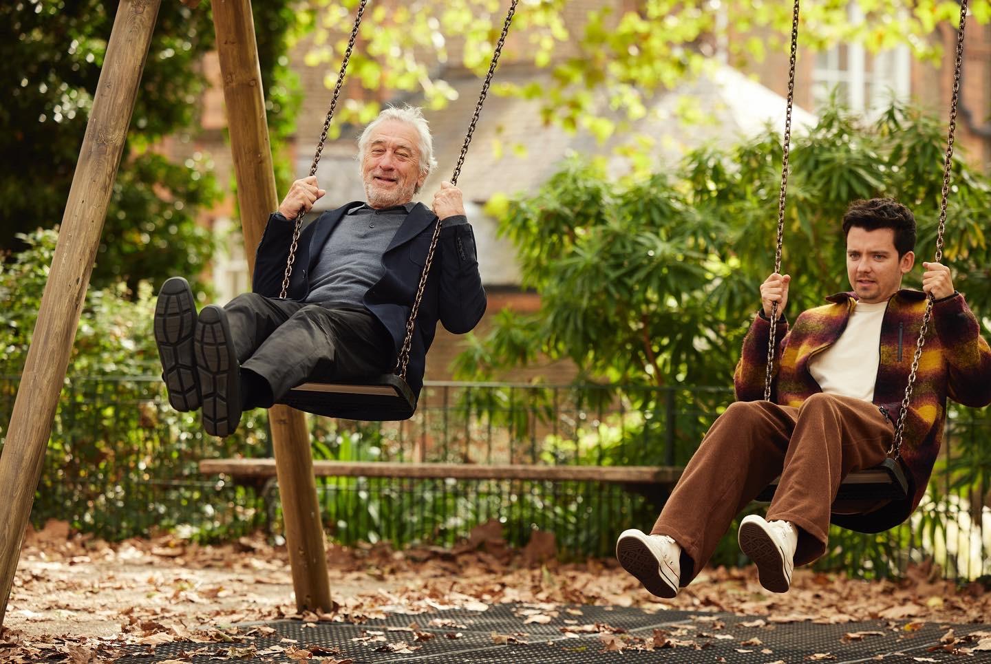 Two men sitting on swings in a park.