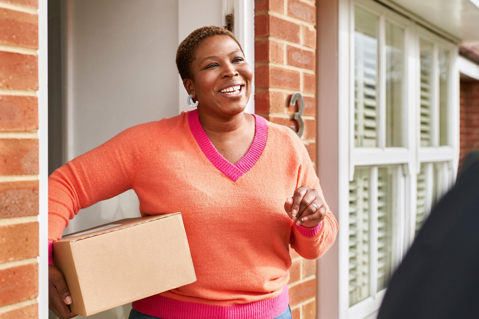 A woman, likely a photographer, standing in front of a brick building, holding a cardboard box and smiling.