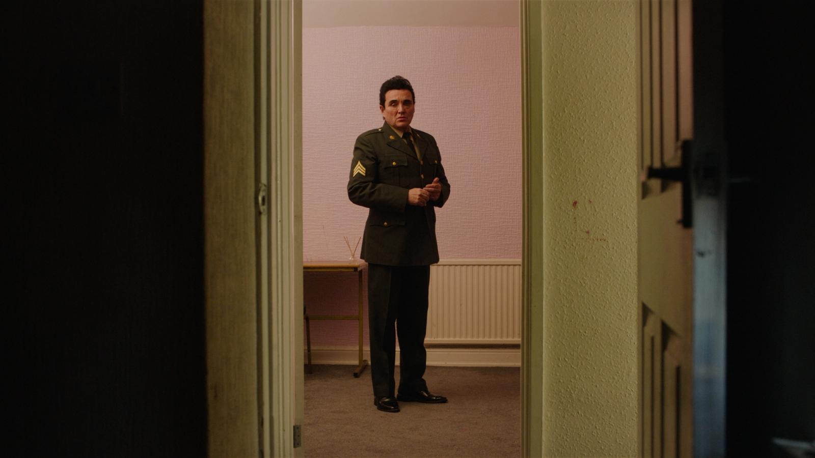 Callum O'Keefe Still from JUAN film, about elvis impersonator in military uniform standing alone in corridor pink and dark