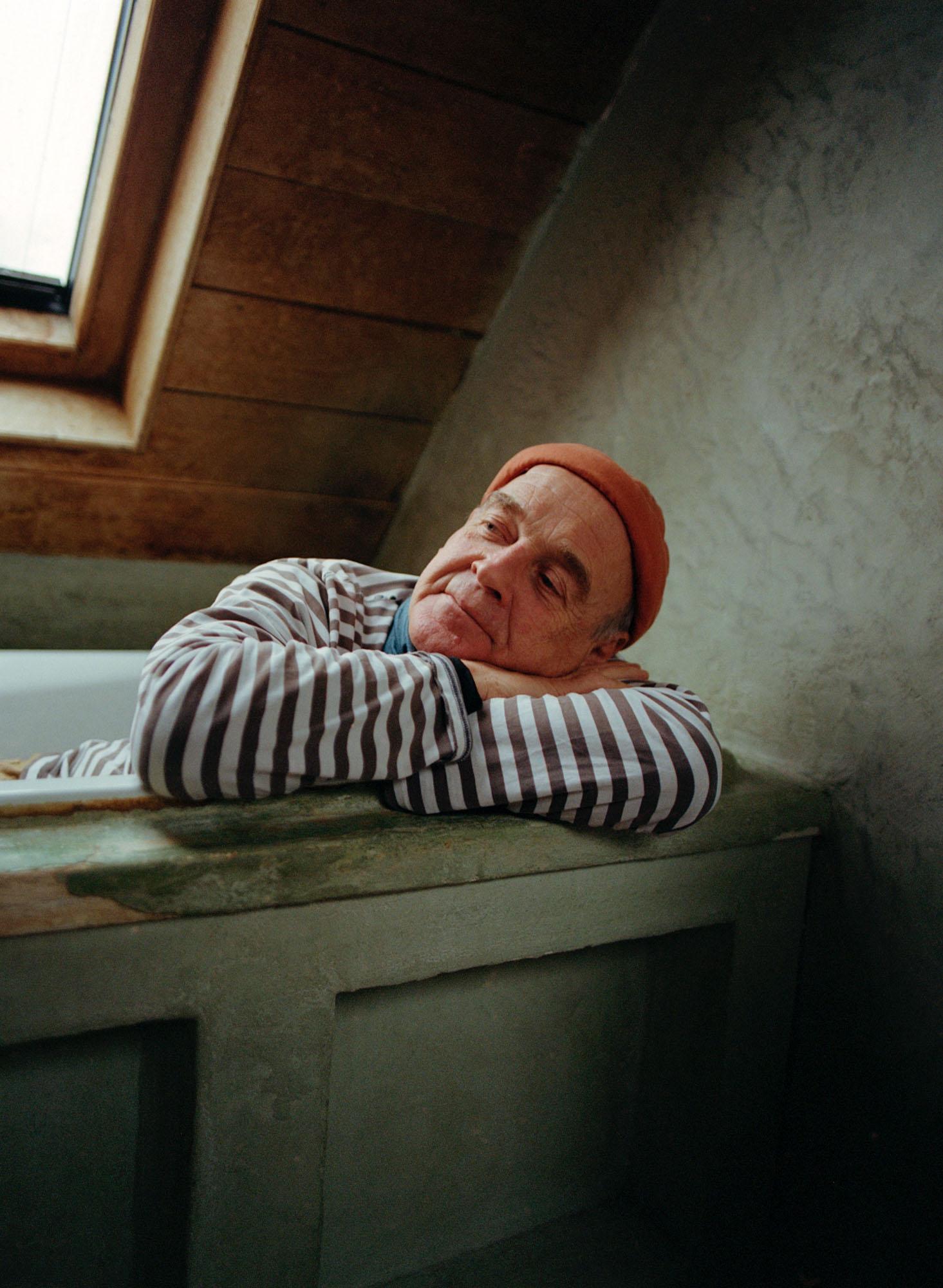 An older man with a red hat and striped shirt is sleeping on a wooden table in a dimly lit room.