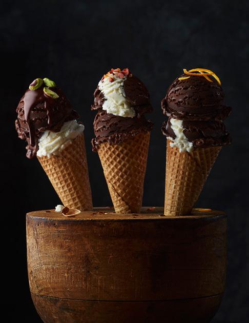 A trio of ice cream cones, each with a different flavor and topping, sitting on a wooden table.
