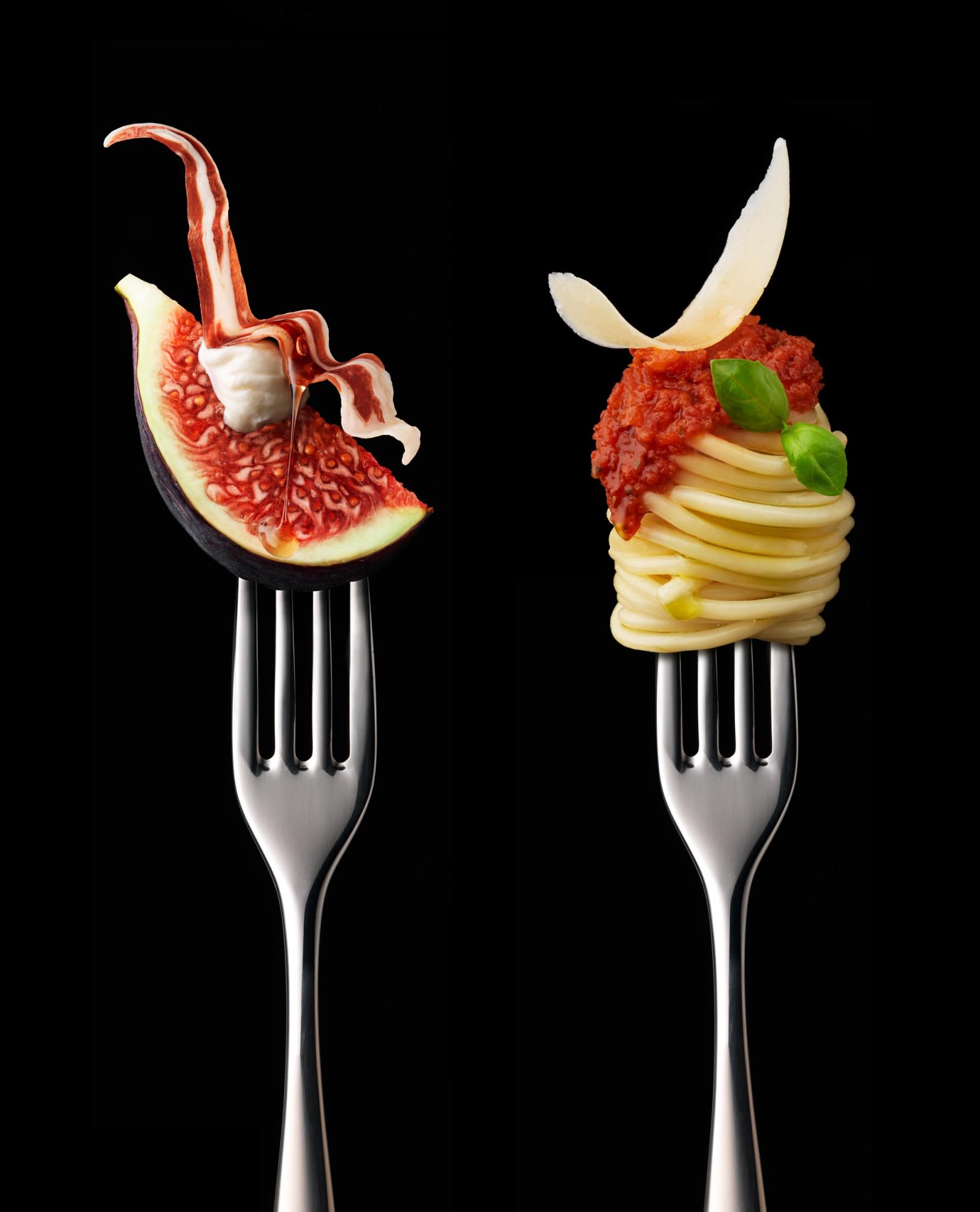 The image features two forks, each with a different food item. On the left, a fork has a slice of fig with a dollop of cheese on top, while on the right, a fork has a twist of.