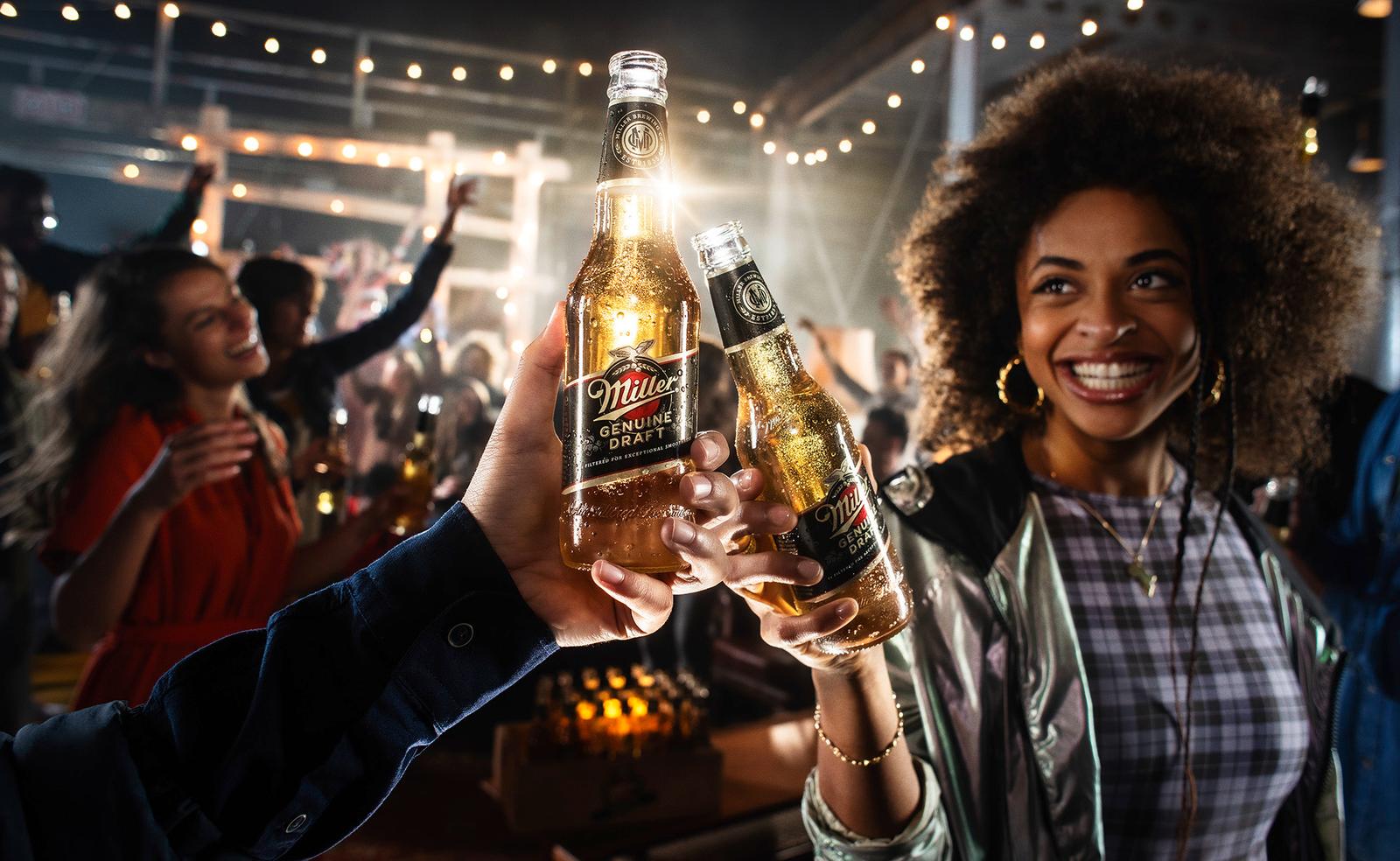 People clinking Millers Genuine Draft beer bottles at an outdoor event.