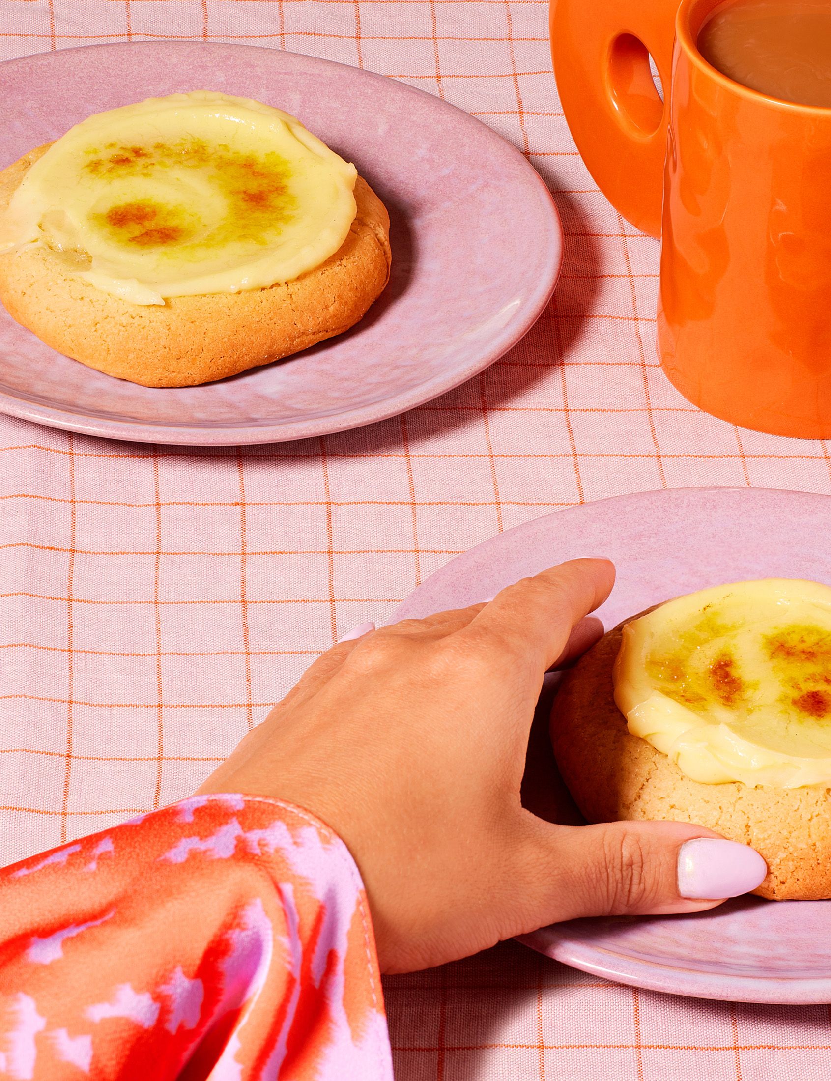 A hand reaching for a cookie on a plate, with a cup of coffee in the background.