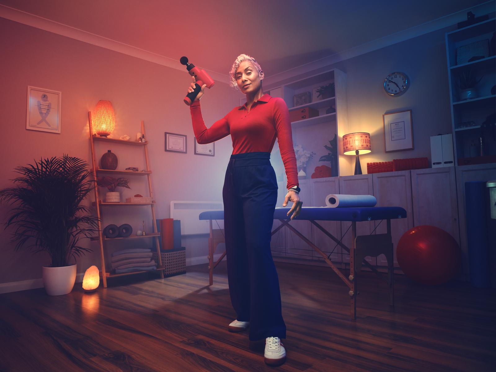 A woman holds a massage gun in a dimly lit room.
