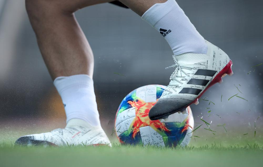 A person's legs in white Adidas socks and cleats, kicking a soccer ball on a grassy field.