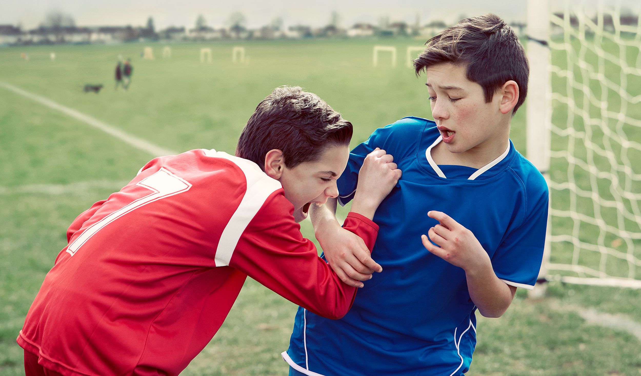 Two young boys in football jerseys standing on a football field.