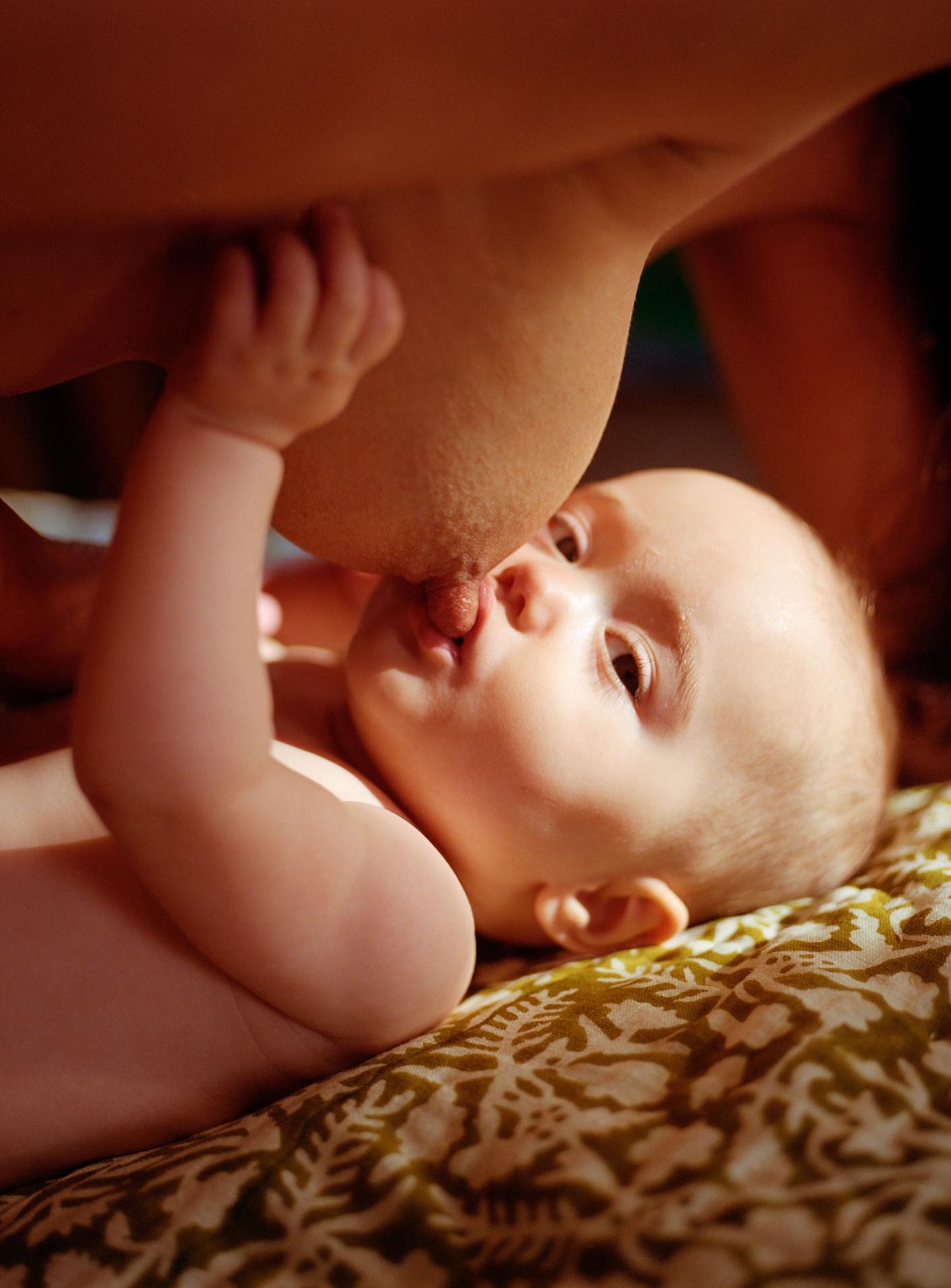 A mother is breastfeeding her baby, with the mother's bare breast and the baby's face visible.