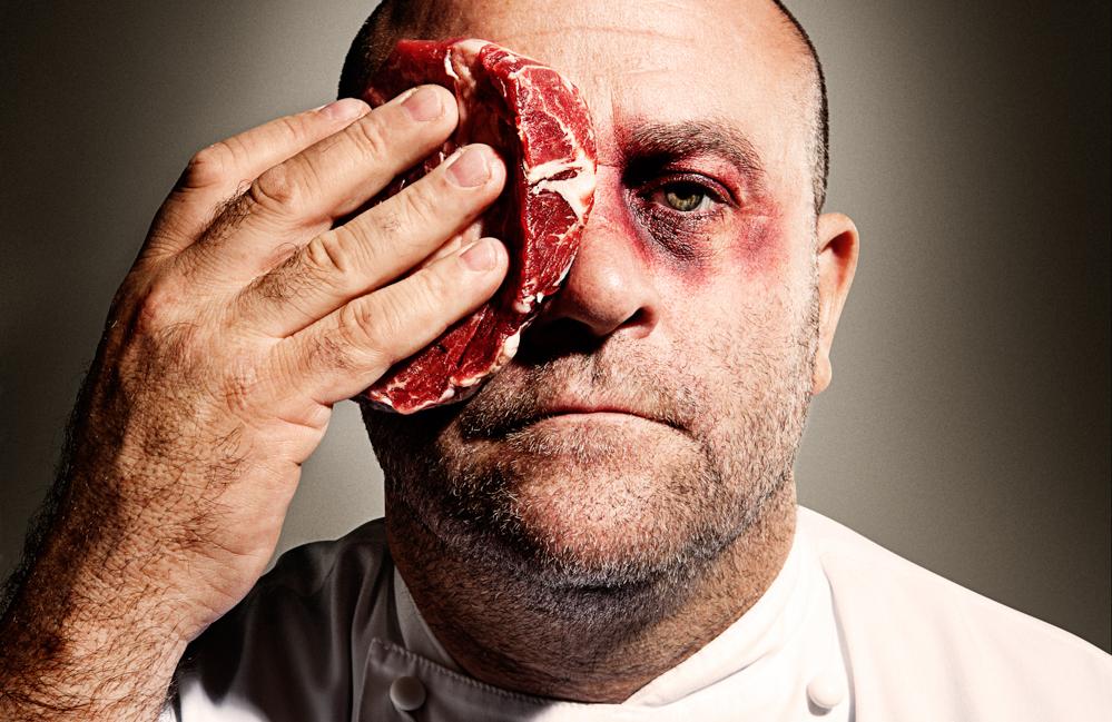 A man wearing a white chef's coat with a steak covering one eye.