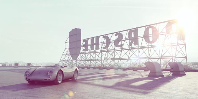 A 1955 Porsche 550 Spyder is parked in front of a large, metal, industrial-style sign reading 'SCHWAB' in bold, black letters.