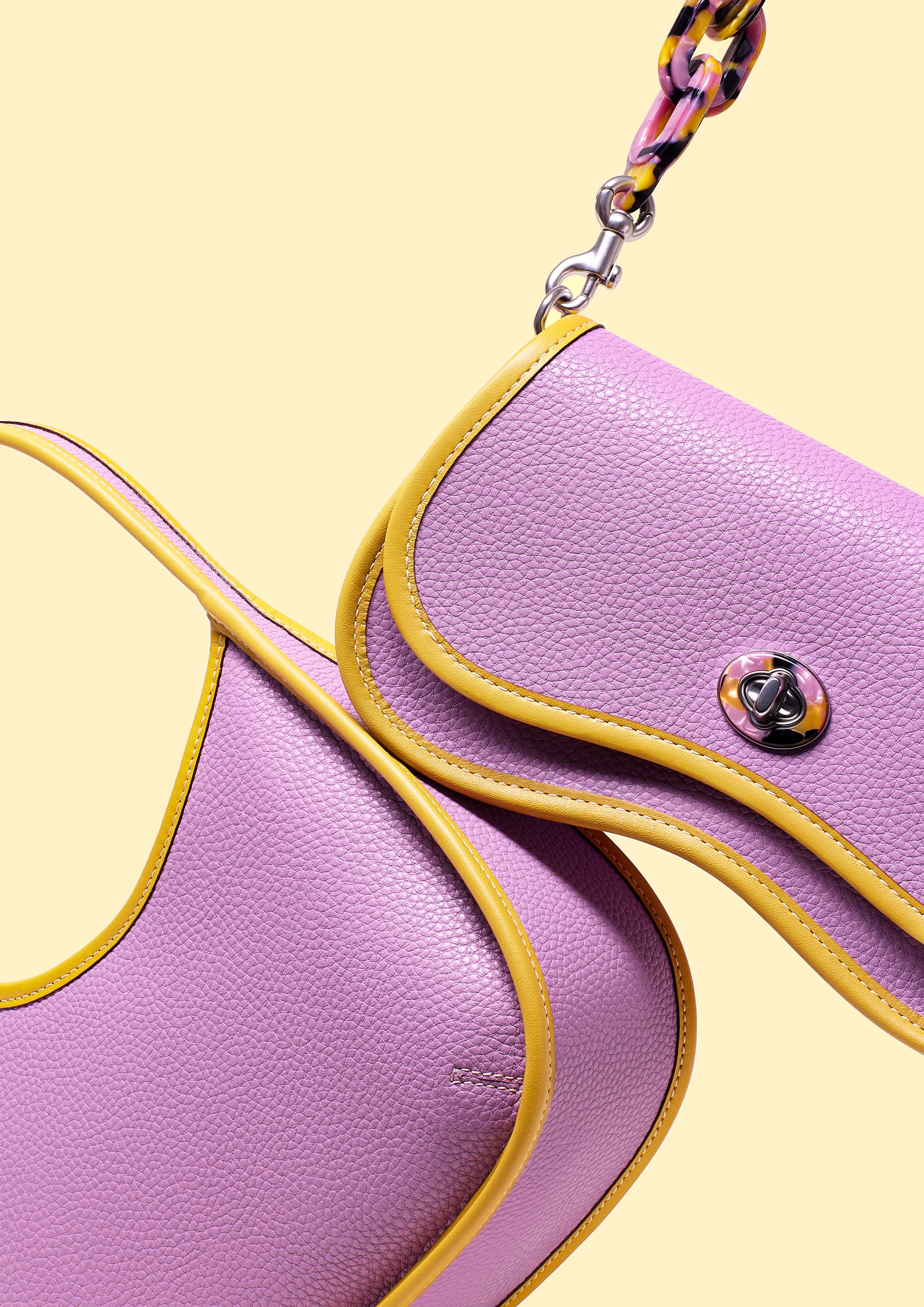 A close-up of a pink leather handbag with a gold chain strap, featuring a small, round, silver clasp.