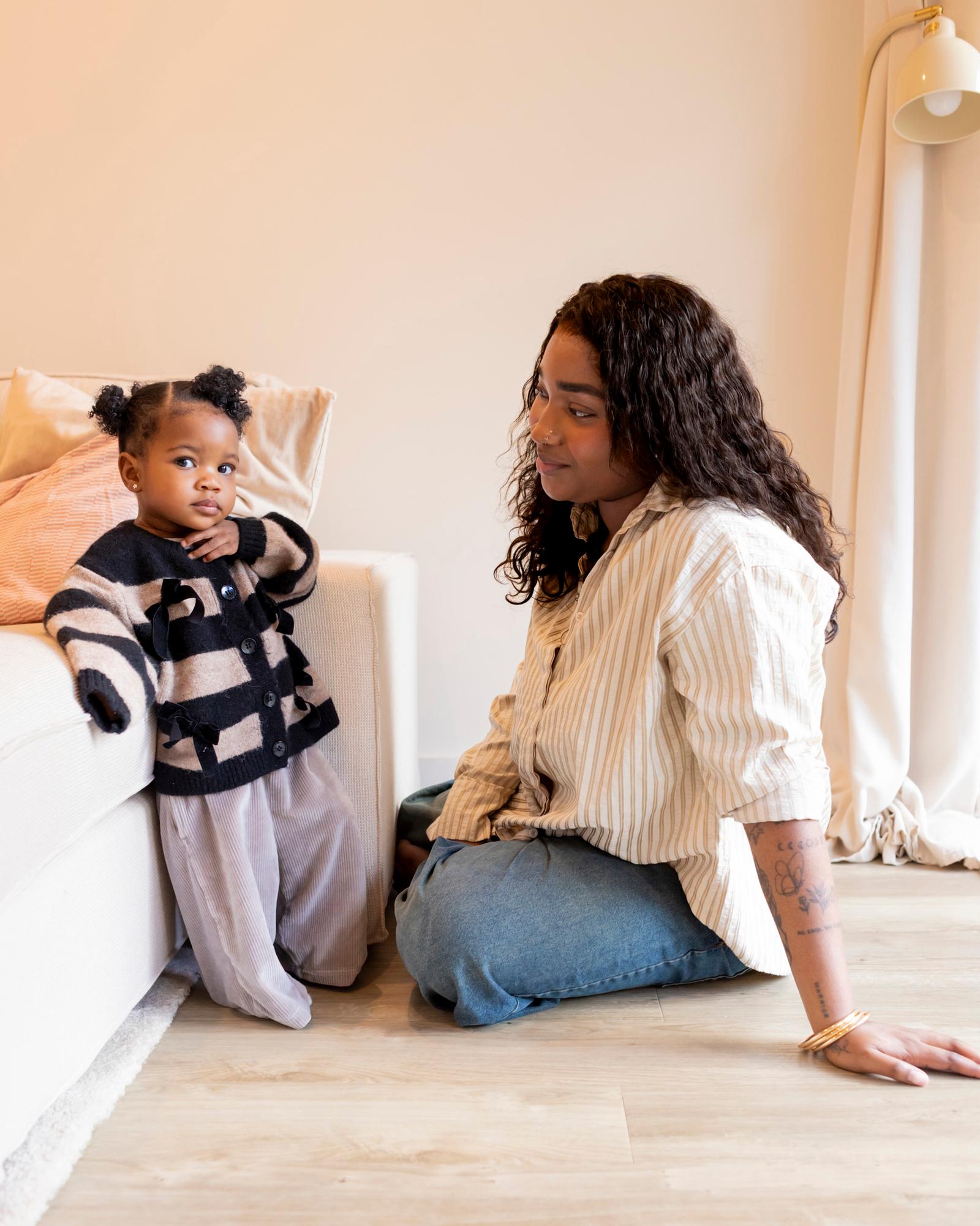 A young woman with a child sitting on the floor in a living room, both looking at something out of frame.