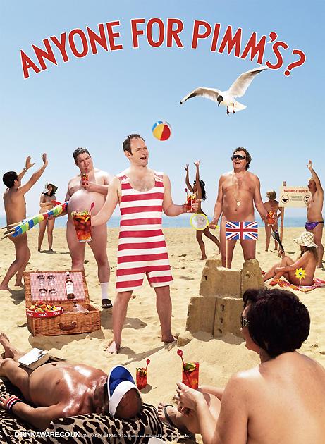 A man holds a drink on a beach with others, a beach ball, and a sign.