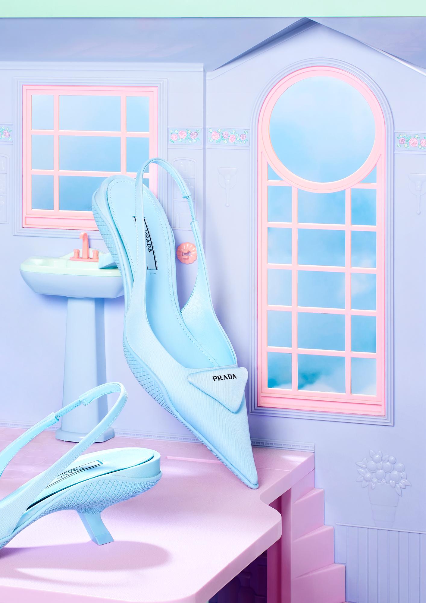 A pair of high-heeled, pointed-toe, slingback shoes in a pastel blue color, sitting on a pink table in a room with a blue and pink color scheme, with a window in the background.