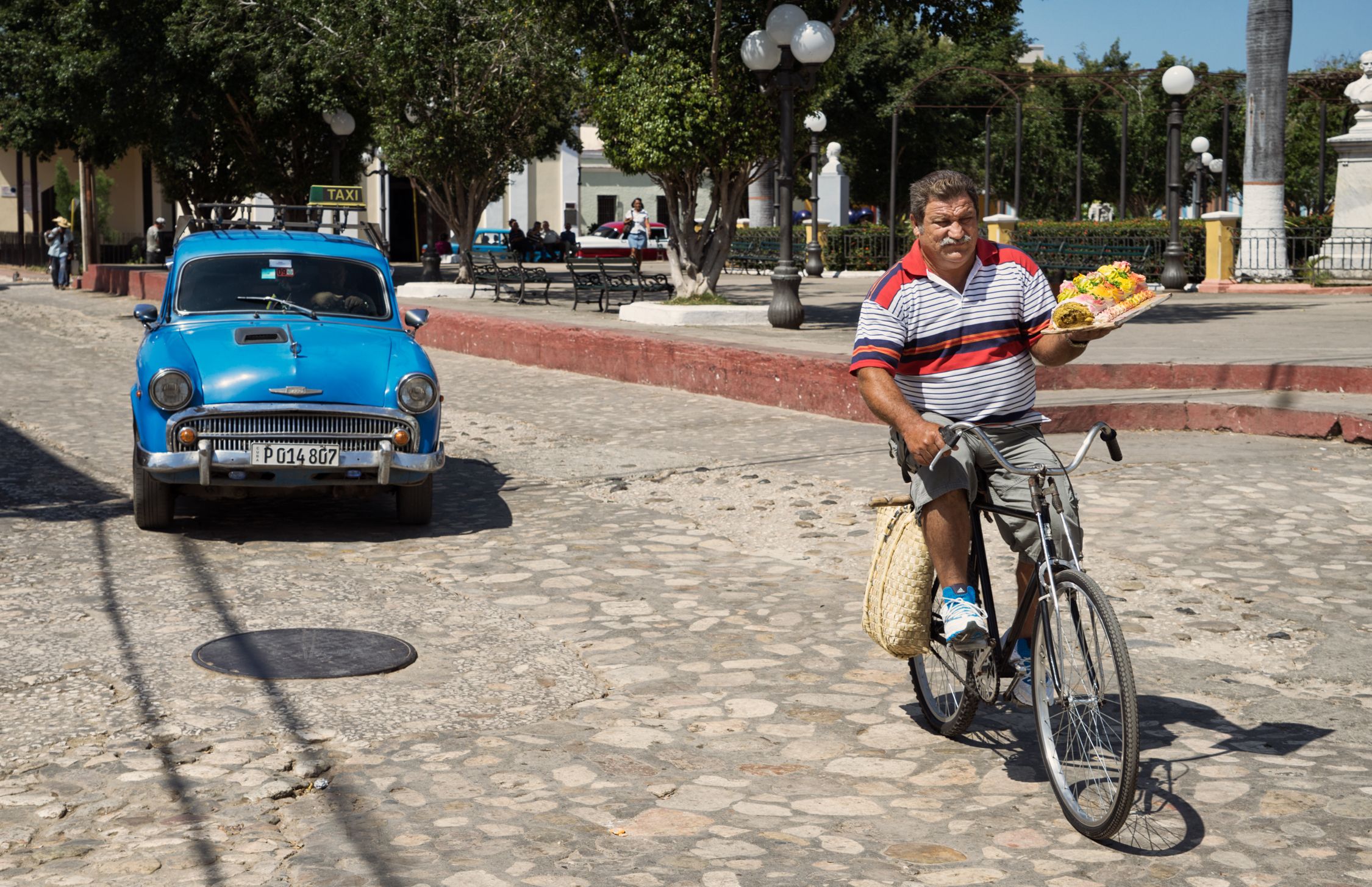 A man on a bicycle holding a pizza in a street.