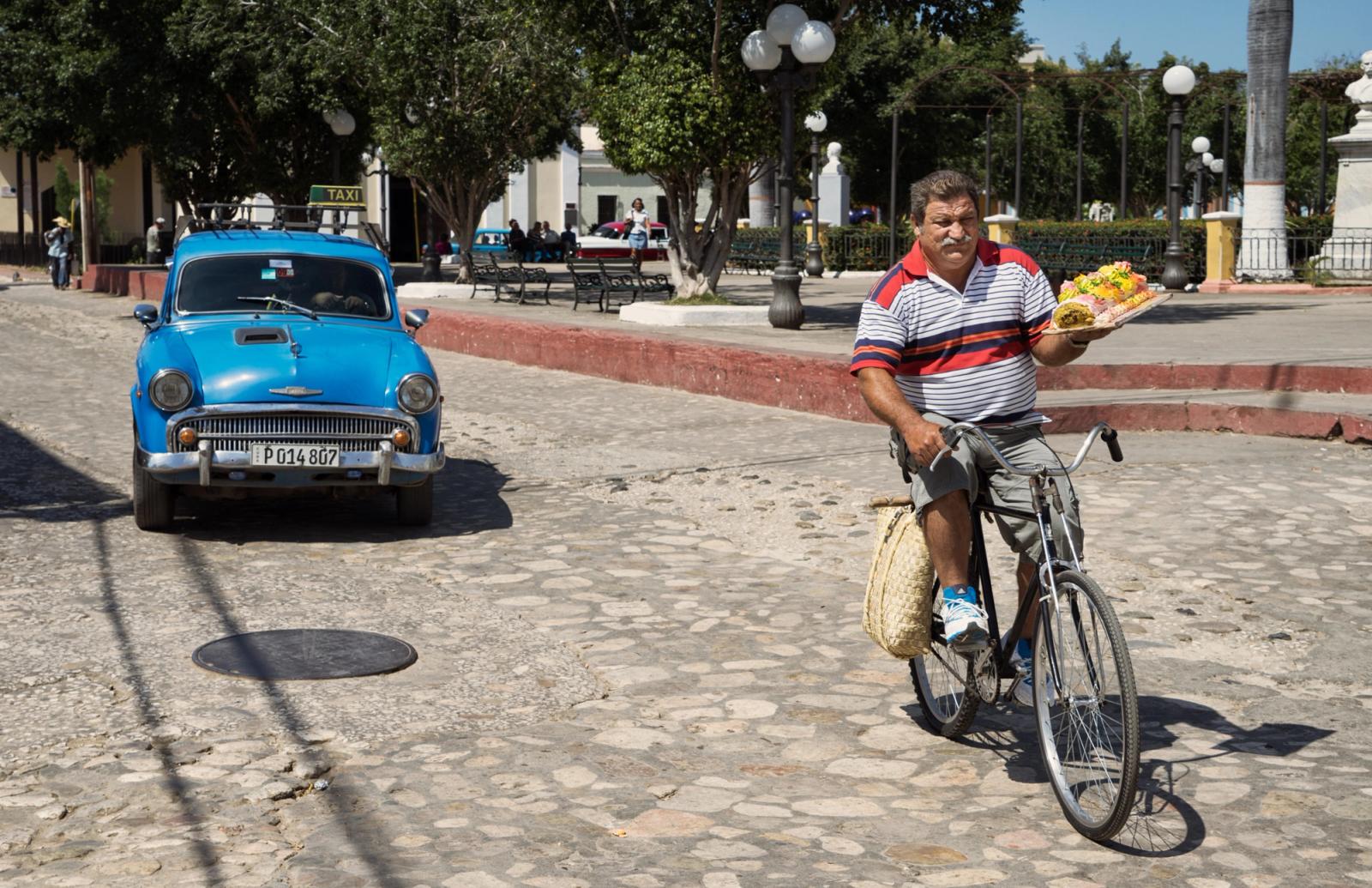 A man on a bicycle holding a pizza in a street.