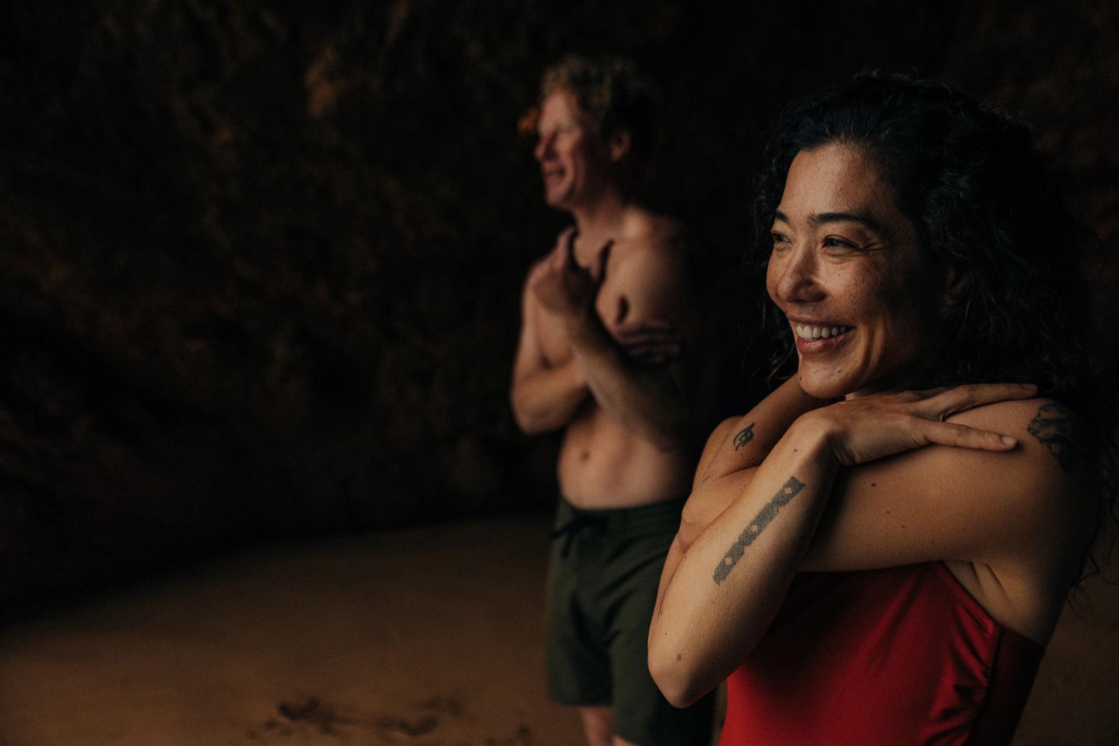 Two people, a man and a woman, embracing and smiling at the beach, both wearing swimsuits.