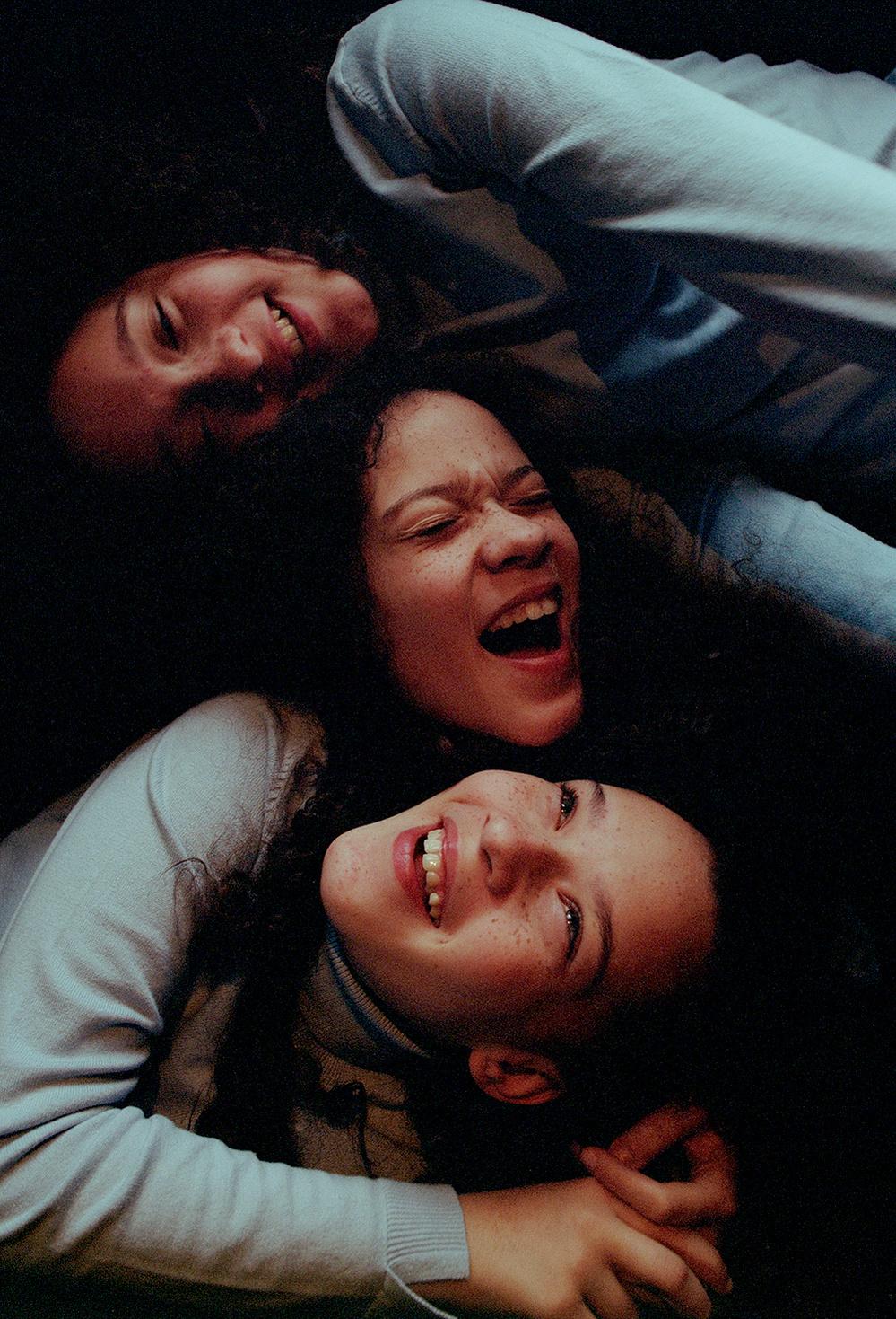 A group of people laughing and hugging each other, with some people lying on the ground and others standing around them, all smiling and having fun.