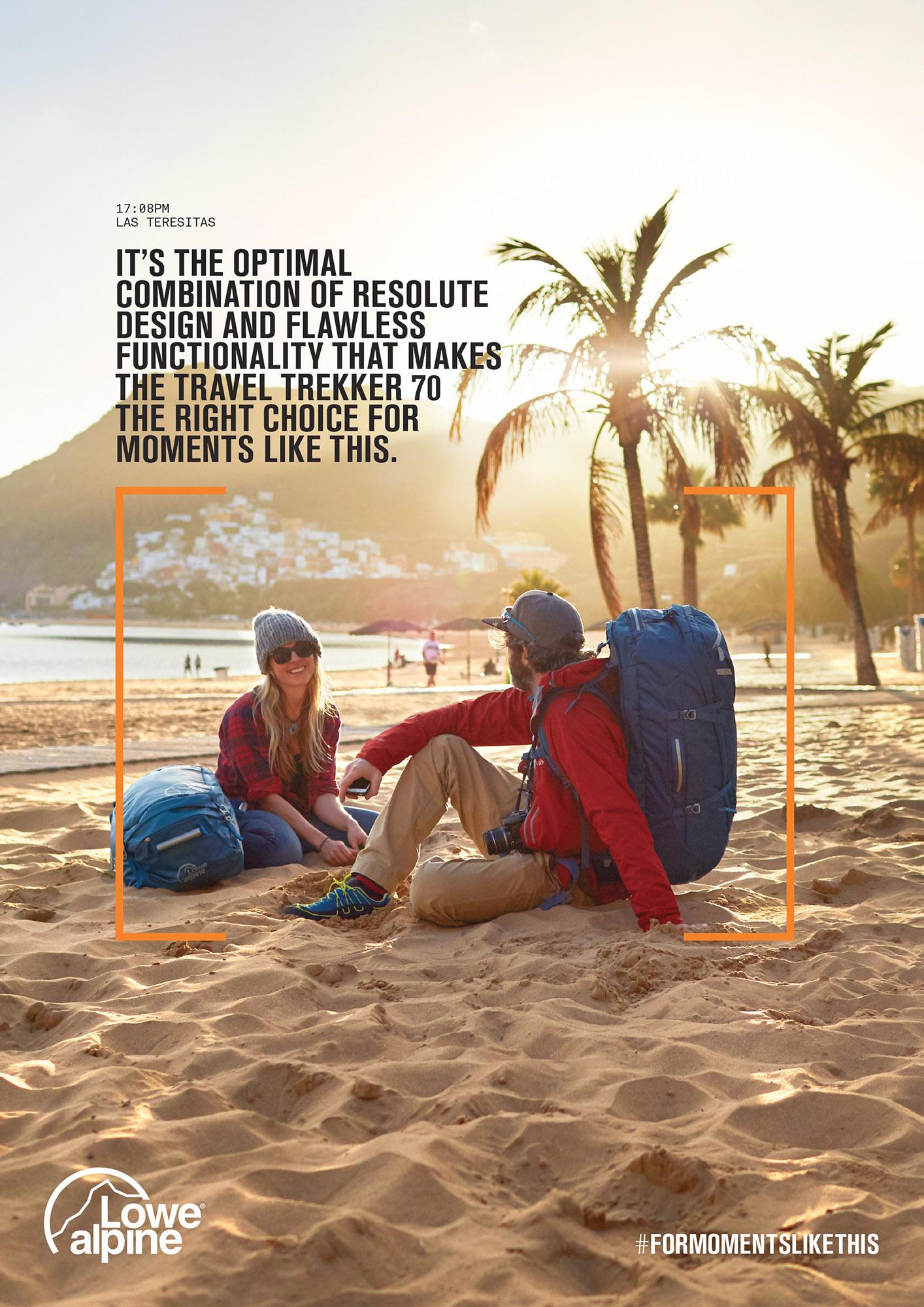 A man and woman sitting on a beach, both wearing red jackets and blue backpacks, with a cityscape in the background.