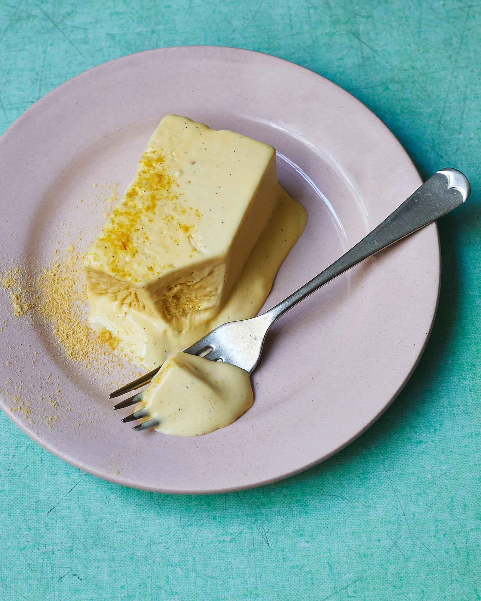 A plate containing a creamy yellow dessert with a fork holding some of the dessert and its sauce.