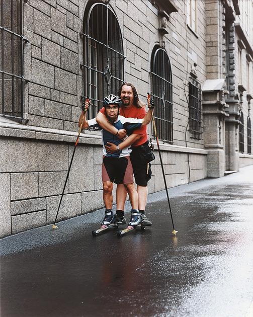 Two men on rollerblades in front of a stone building.