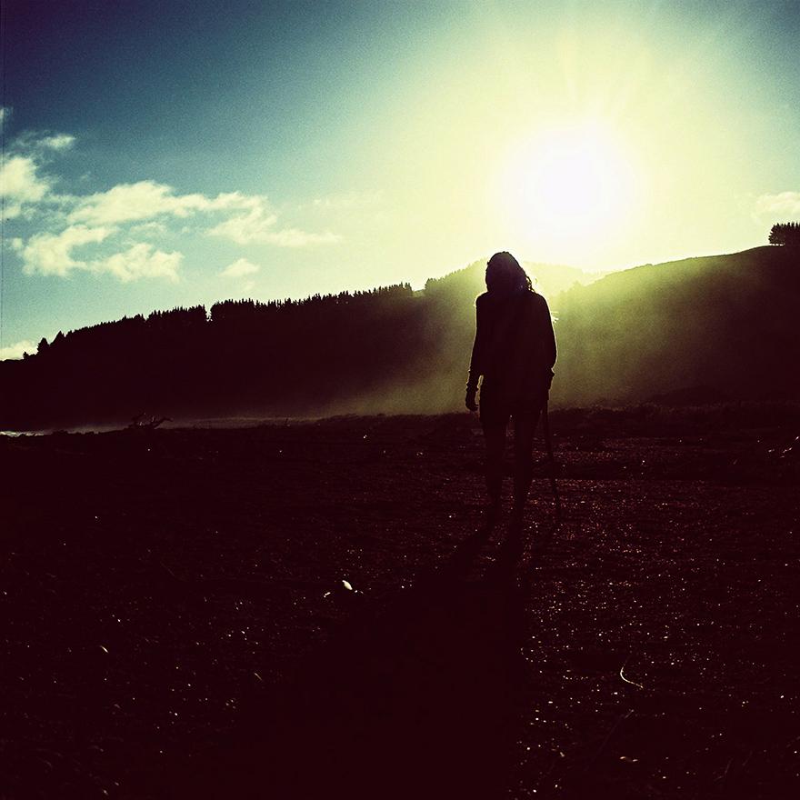 A woman standing alone on a beach at sunset, with the sun's rays casting a golden glow on her face and the surrounding landscape.