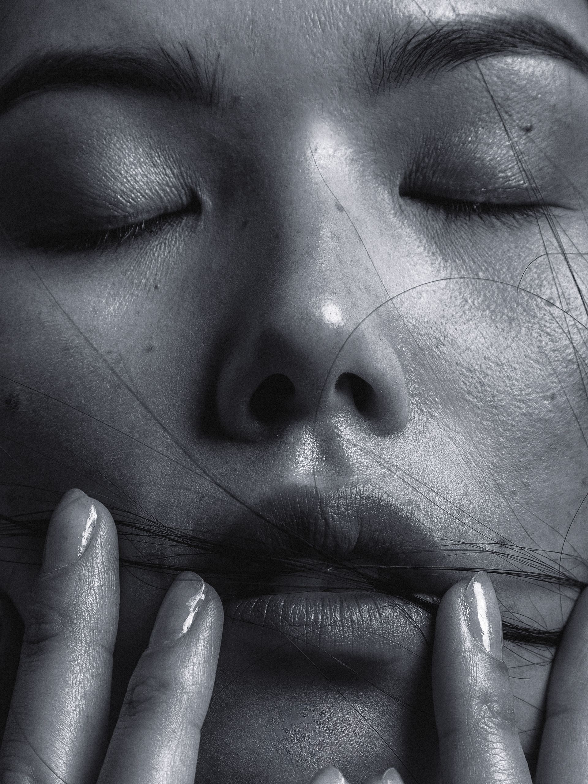 A close-up of a woman's face, with her eyes closed and her lips slightly parted, with a few strands of hair in front of her mouth.