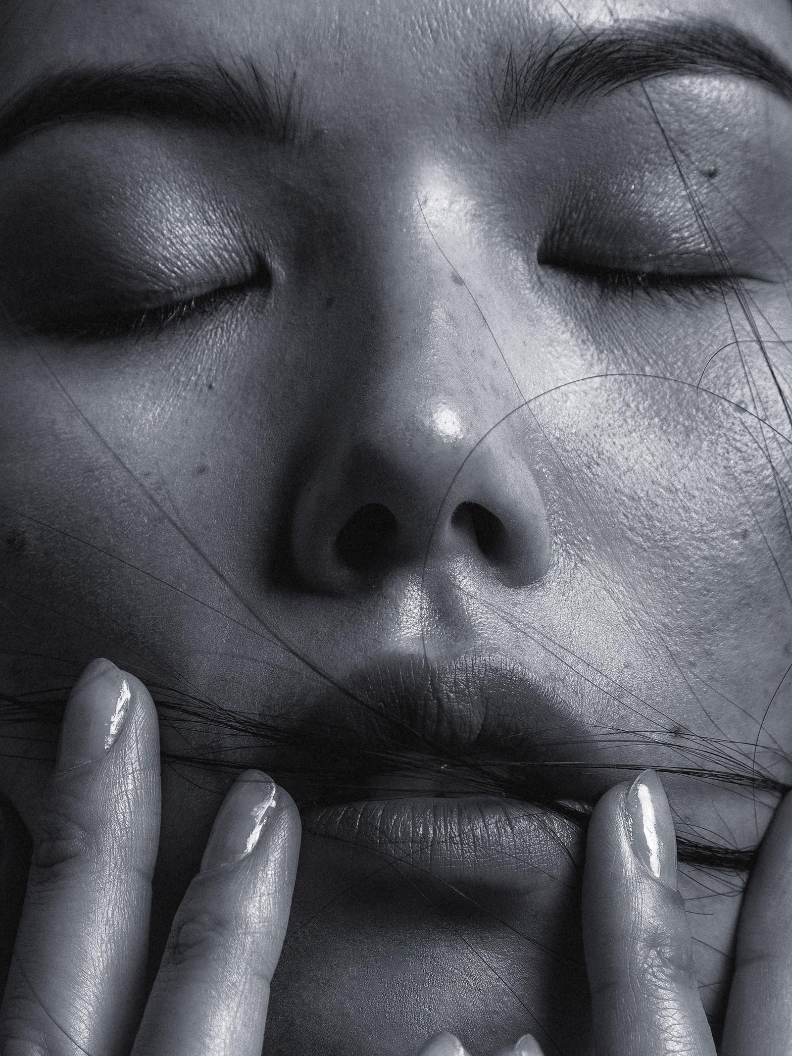 A close-up of a woman's face, with her eyes closed and her lips slightly parted, with a few strands of hair in front of her mouth.