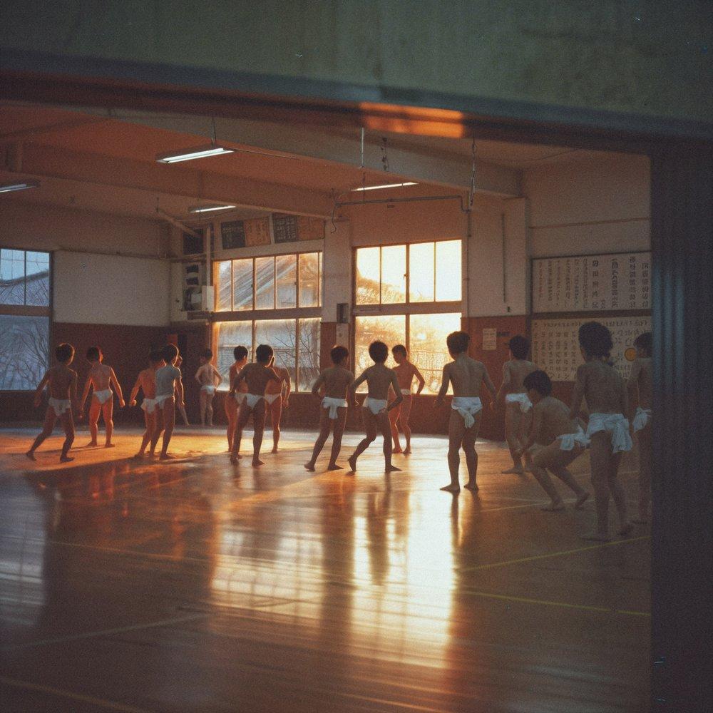 A group of young children, likely in a school setting, are seen in their underwear, standing in a large, empty room with a high ceiling and large windows.