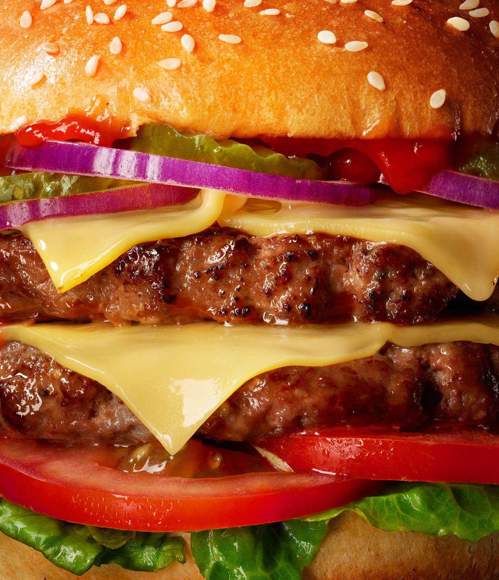 A juicy, high-quality burger with multiple layers of ingredients, including a beef patty, cheese, lettuce, tomato, and red onion, all served on a toasted, sesame-seed bun.
