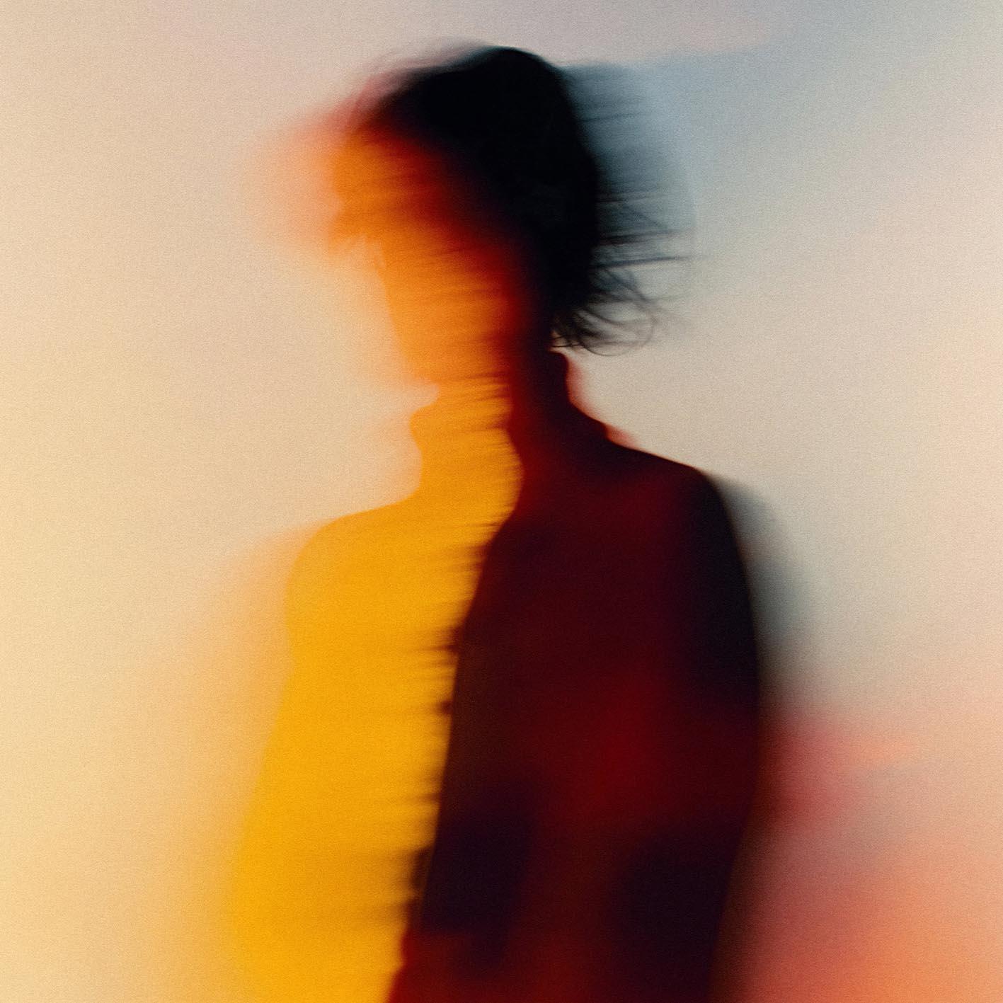 A woman in a white shirt with a subtle, shimmering fabric that catches the light, standing in front of a blurred, urban background.