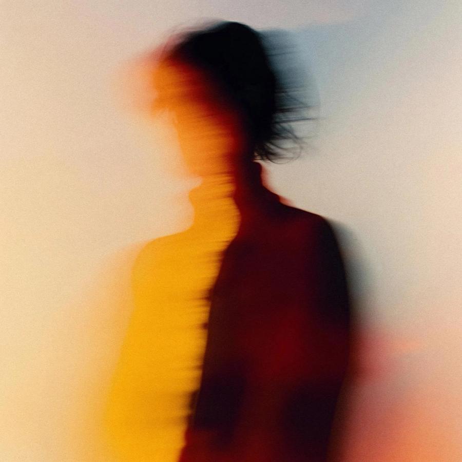 A woman in a white shirt with a subtle, shimmering fabric that catches the light, standing in front of a blurred, urban background.