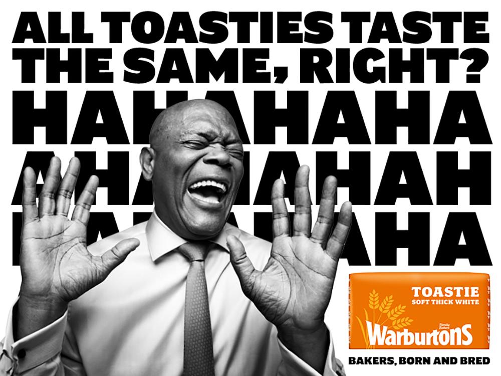 A man in a suit and tie laughing while holding up a toastie.