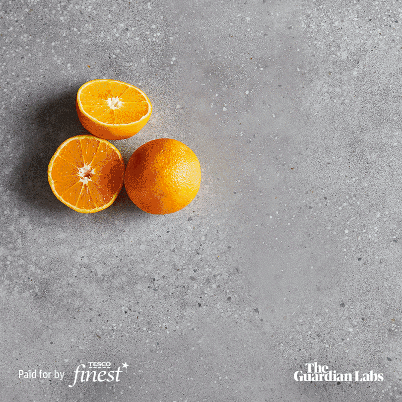 Three oranges, one of which is cut in half, on a grey surface.