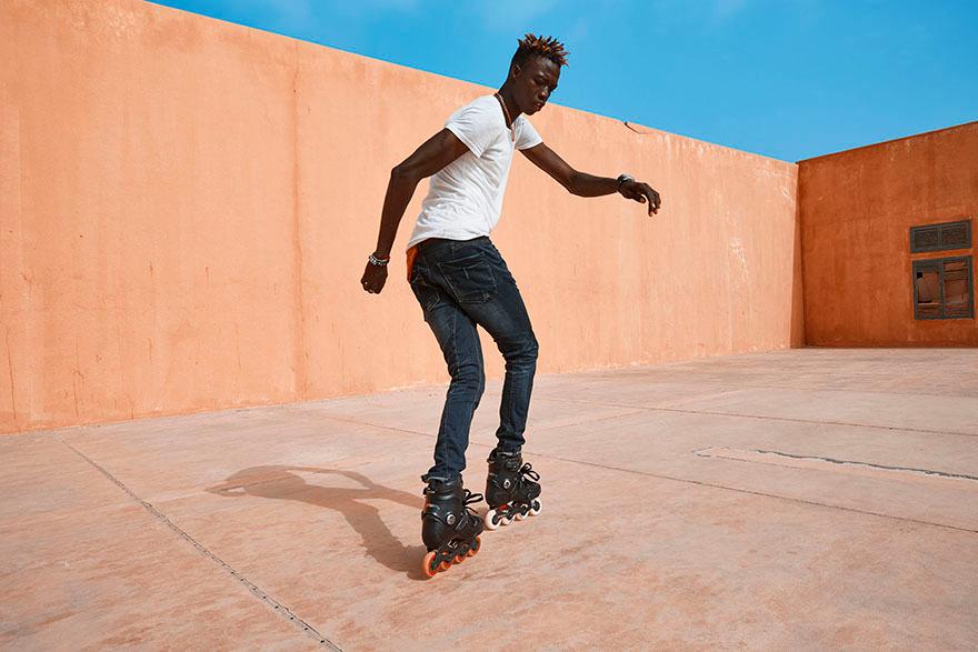 A man in a white t-shirt and dark jeans rollerblading in an empty, orange-painted courtyard.