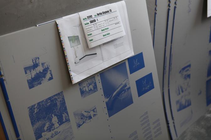 A collection of printed images on a wall, with a whiteboard in the background displaying a list of images to be printed.