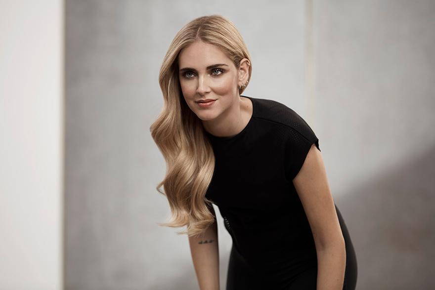 A woman with long blonde hair and a black dress, posing in a studio setting.