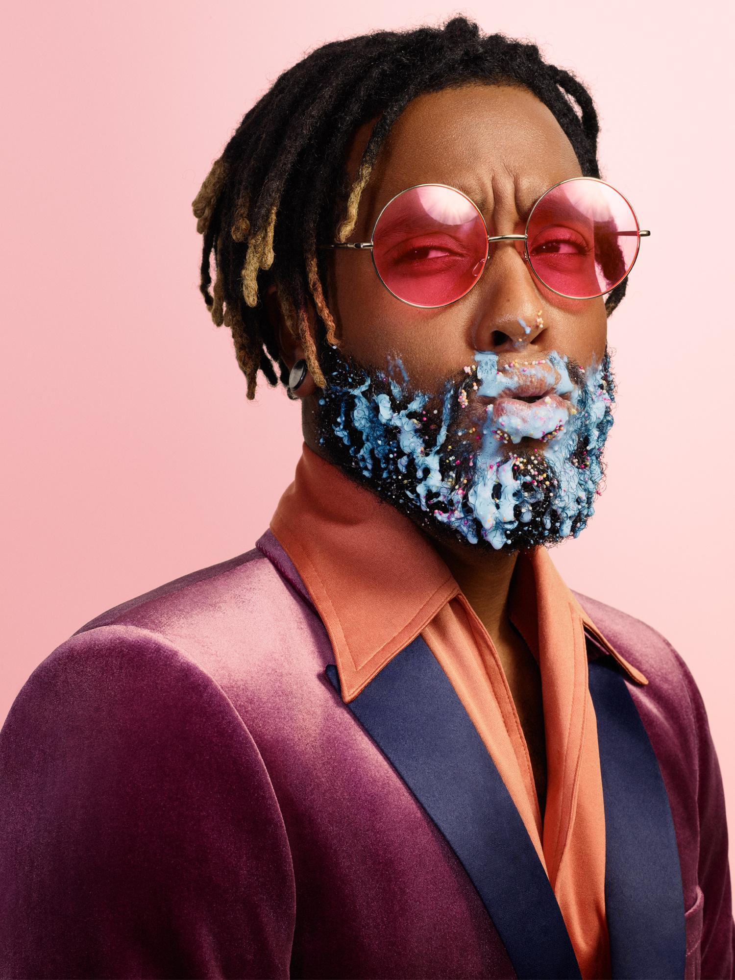 A man with a beard made of colorful, sugary, and messy food items, including candy, ice cream, and cake, with a look of surprise and a bit of mess on his face.