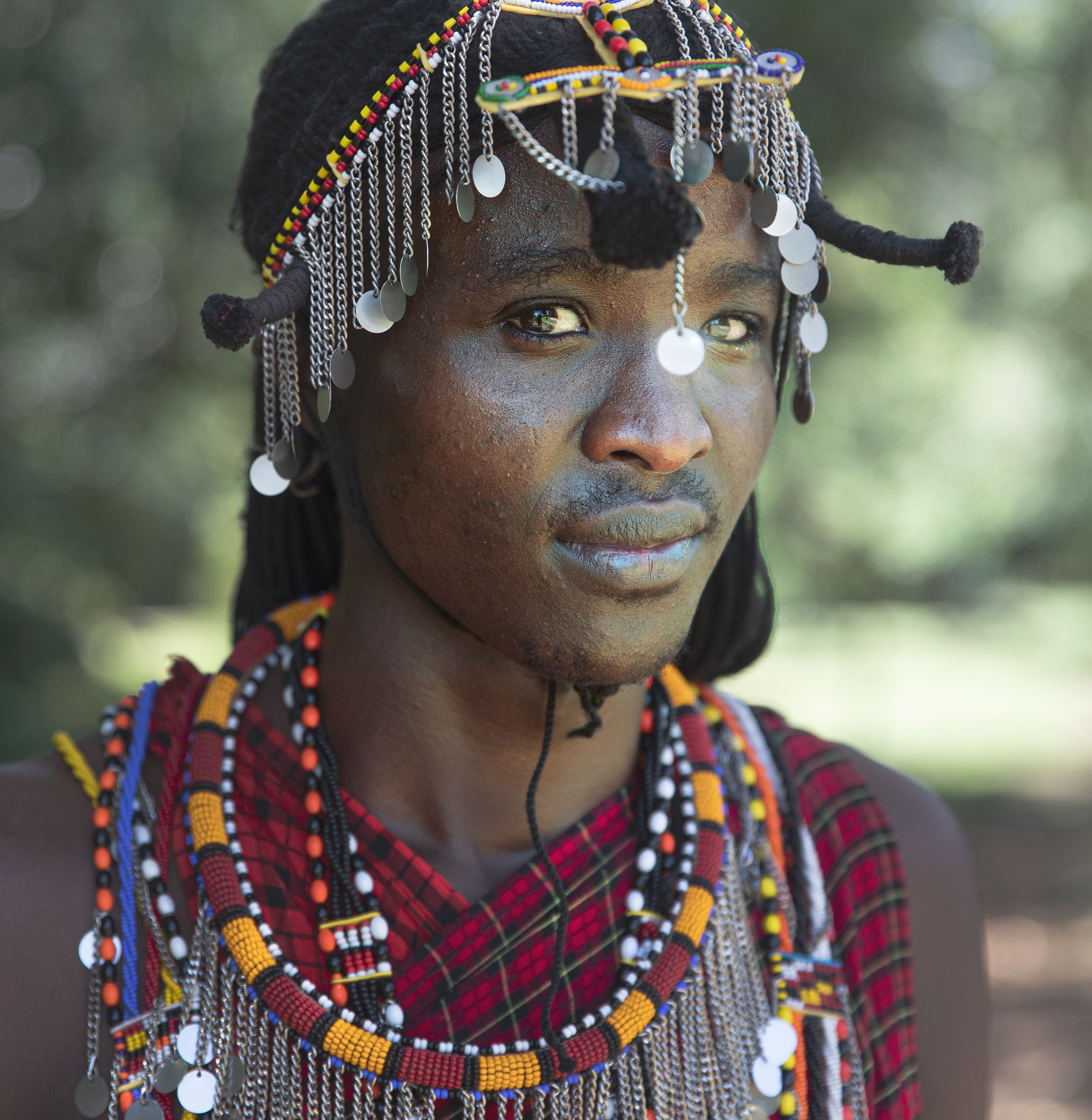 A young African man with a traditional headdress and multiple colorful necklaces and beads.