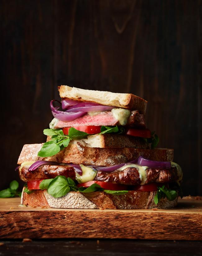 A towering sandwich with multiple layers of ingredients, including meats, cheeses, vegetables, and condiments, all stacked high on a crusty bread loaf.