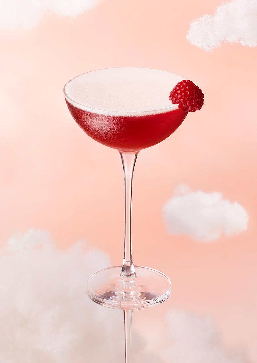 A cocktail glass filled with a red, fruity drink, garnished with a raspberry.