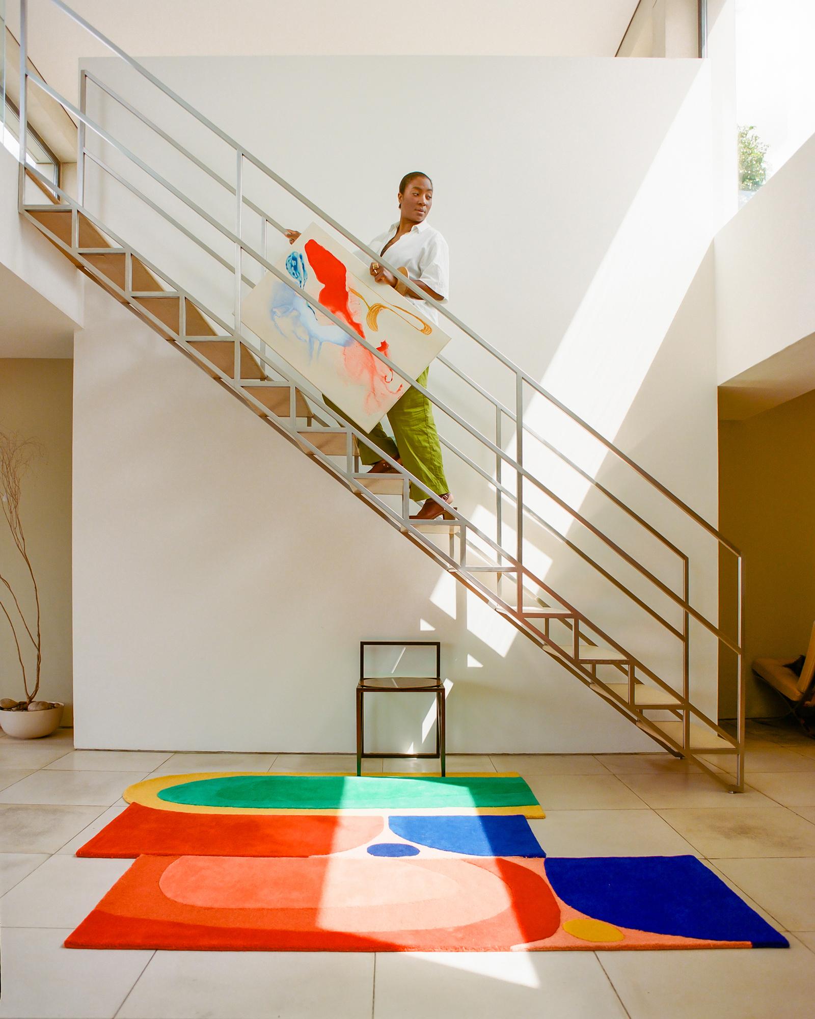 A woman stands on a staircase holding a large painting.