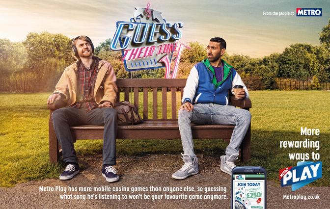 Two men sitting on a bench in a park, one wearing a yellow jacket and the other wearing a blue jacket, both looking at a phone screen