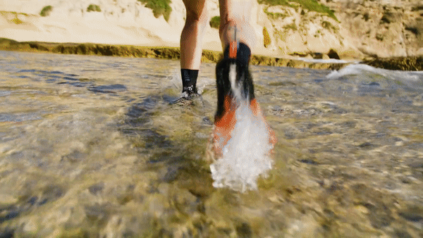 A person is wading through shallow, clear water, wearing a wetsuit and a pair of flippers.