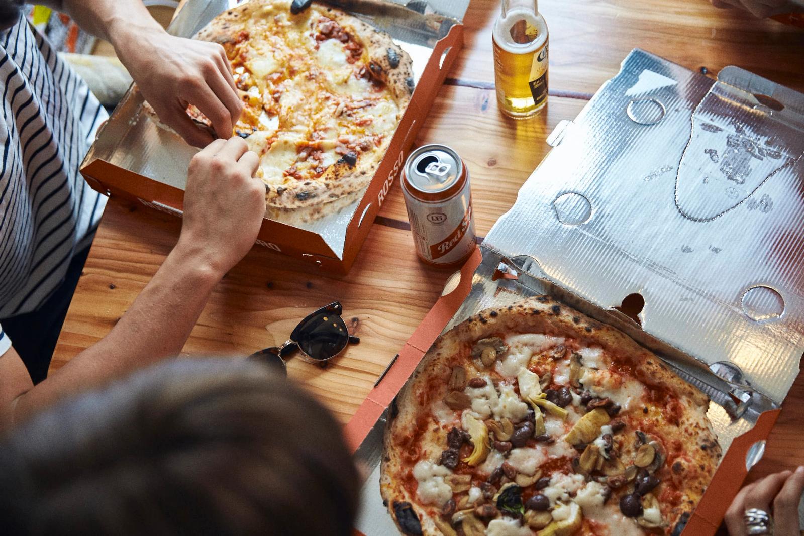 A group of people enjoying pizza and drinks at a table. The atmosphere is casual and social, with people laughing and having fun.