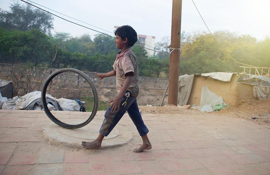 A young boy is playing with a large, old, worn-out tire in a backyard or a similar outdoor setting.