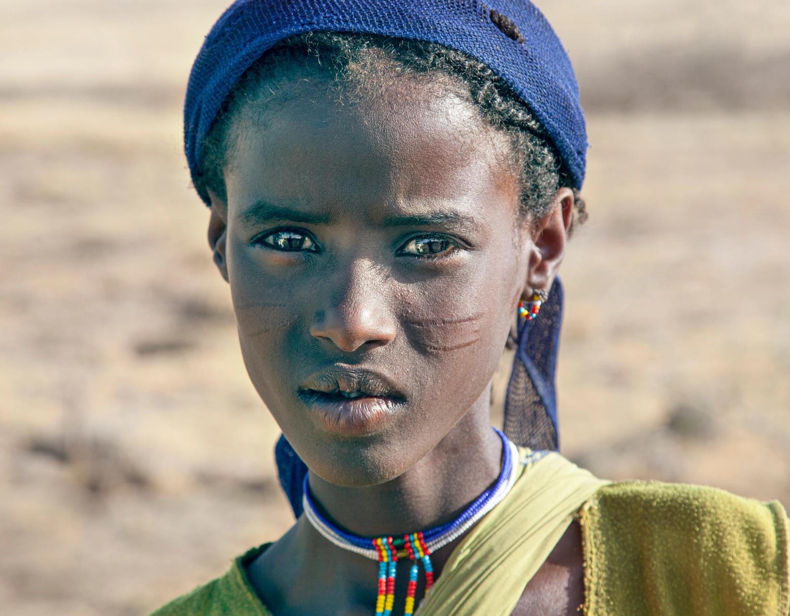 A young girl from the Hamar tribe in Ethiopia, wearing a traditional headdress and a yellow tunic.
