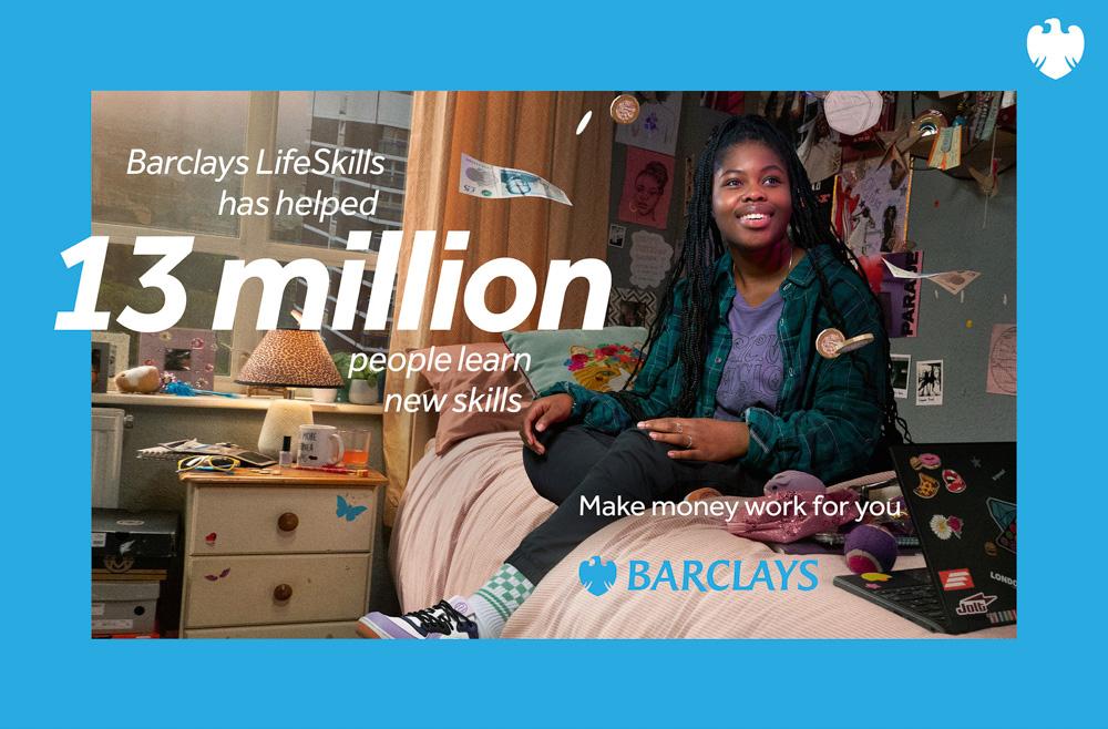 A young woman with long braids sits on a bed in a cluttered bedroom, surrounded by posters and books, wearing a green plaid shirt, black jeans, and sneakers.