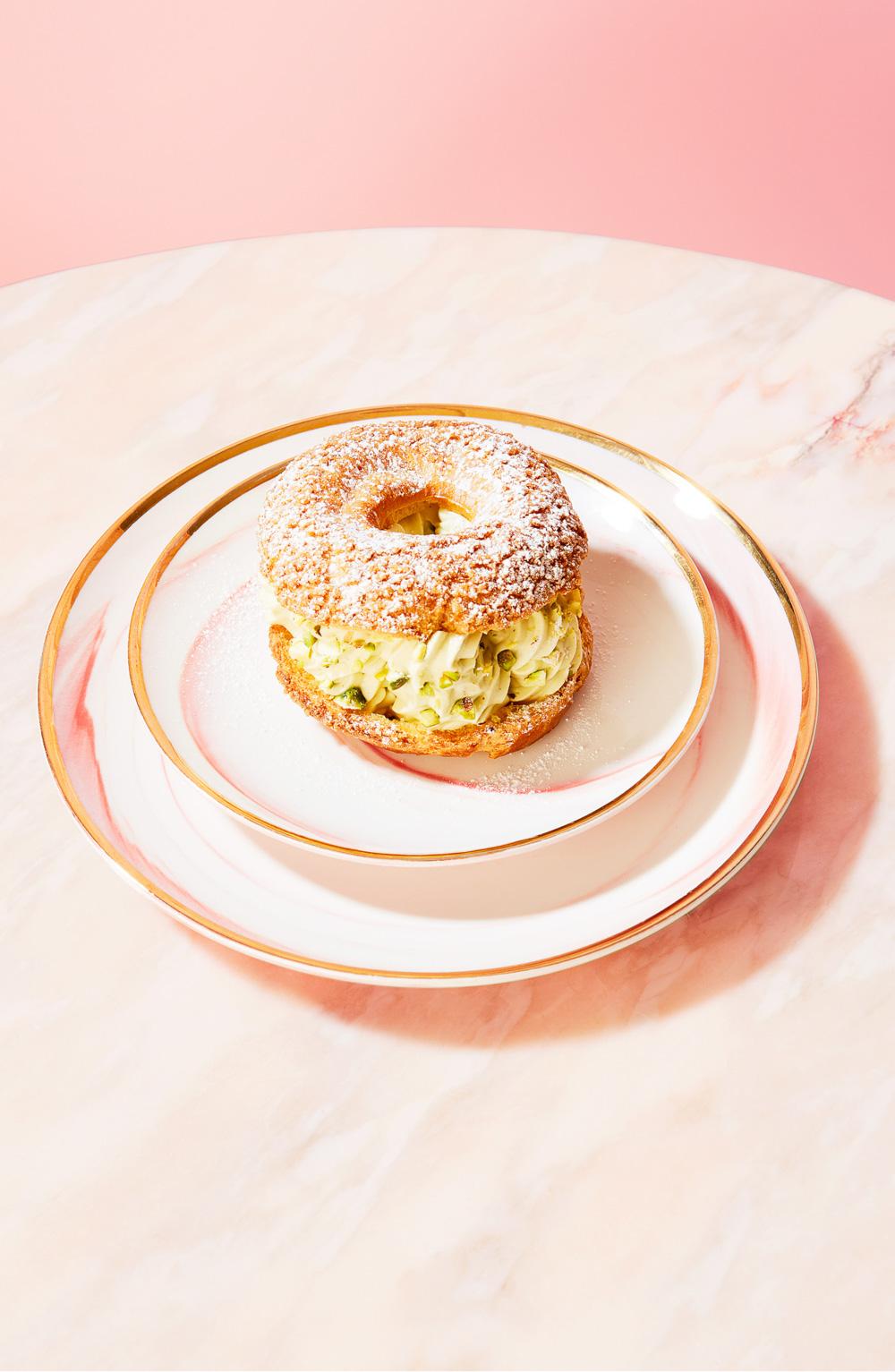 A golden ring-shaped pastry with cream filling on a white plate on a pink marble table.