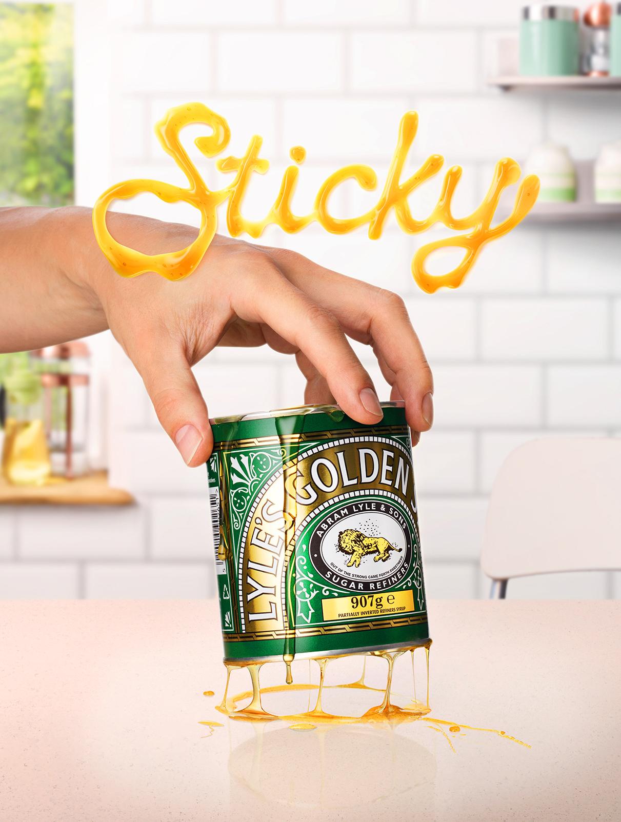 A hand touching a can of Lyle's Golden Syrup with spilled syrup forming a golden liquid.